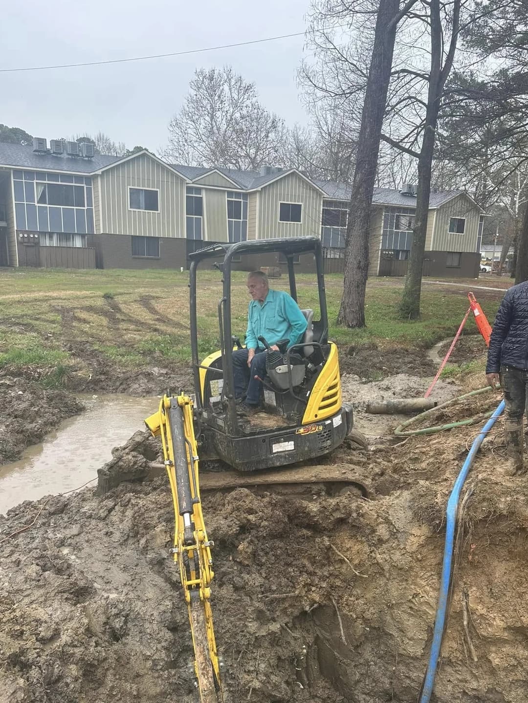 Excavator operator working the trench while a Victory plumber guides the dig