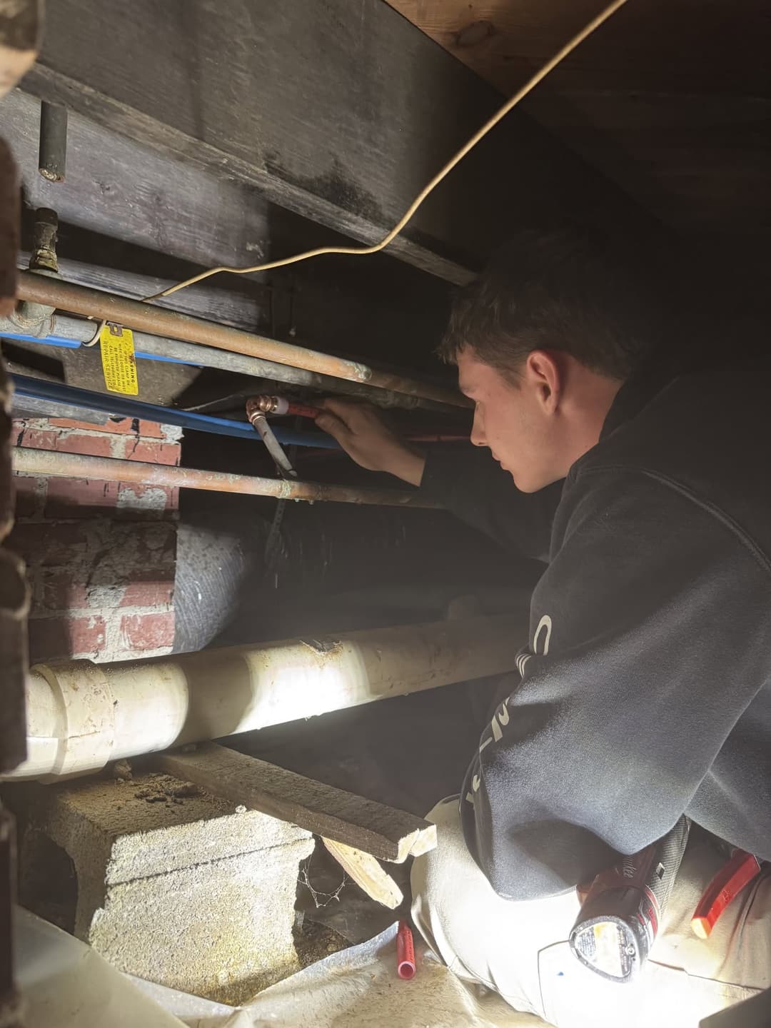 A Victory plumber connects new PEX water lines among the old copper pipes in a crawlspace