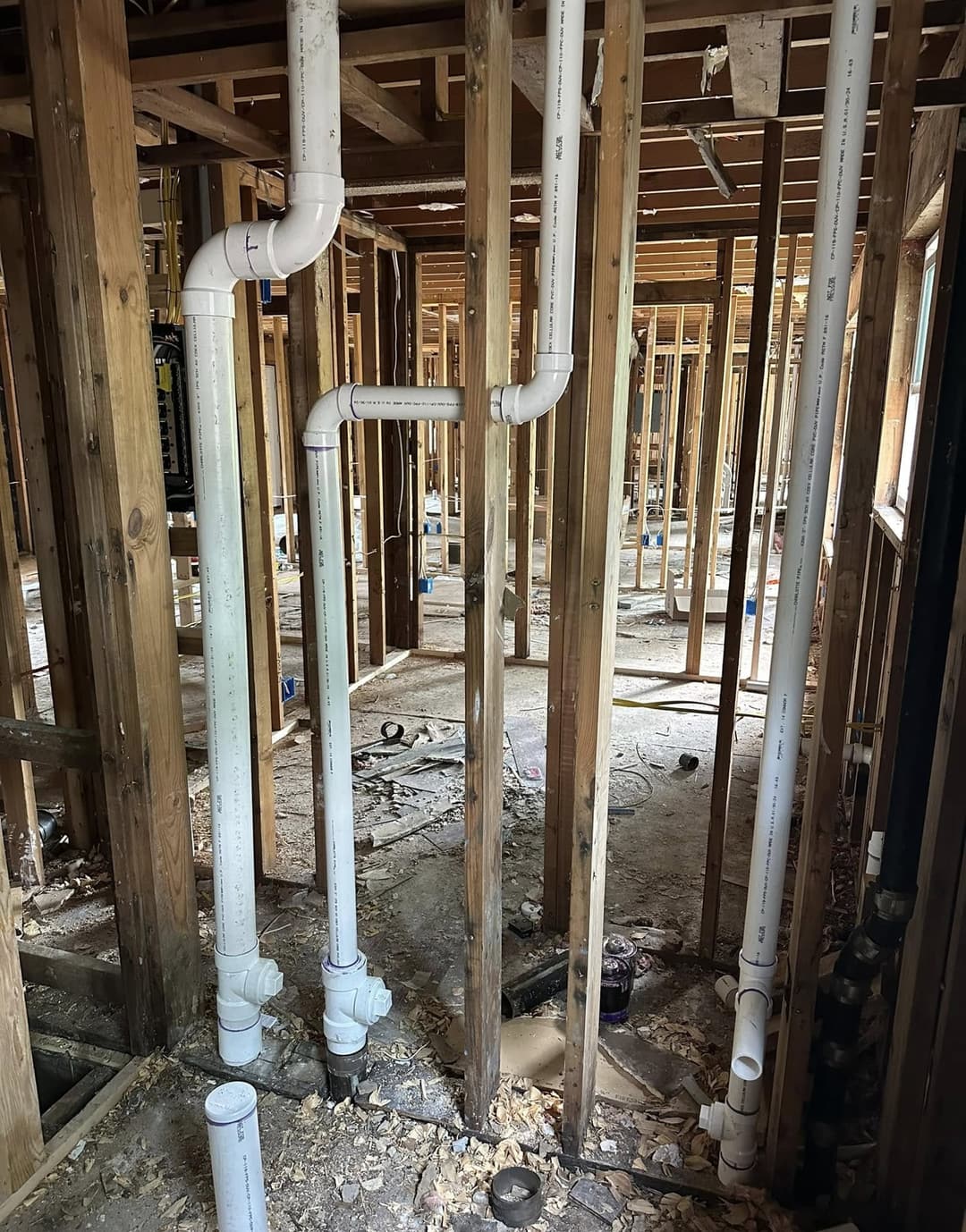 New PVC drain and vent lines with cleanouts in an open-framed house, beside the old cast iron drain