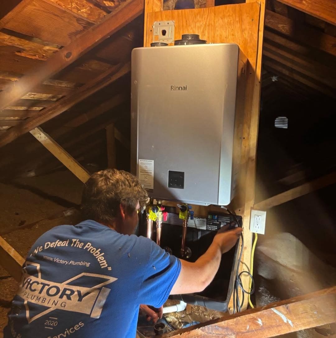 A Victory plumber connecting the water lines on a new Rinnai tankless water heater in an attic